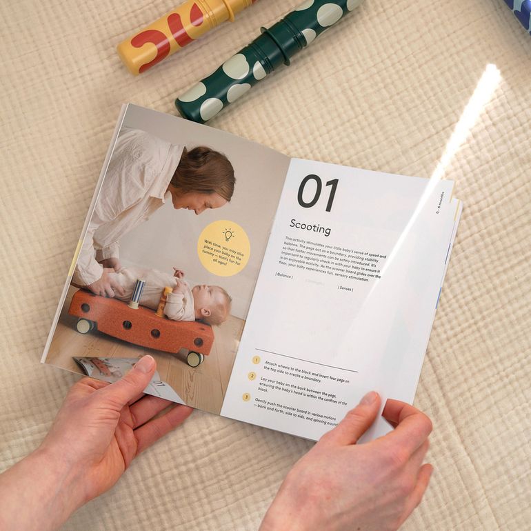 MODU Baby Activity Set handleiding opengeslagen op pagina 01 'Scooting' met handen vasthoudend, bovenop neutrale ondergrond met speelset-accessoires