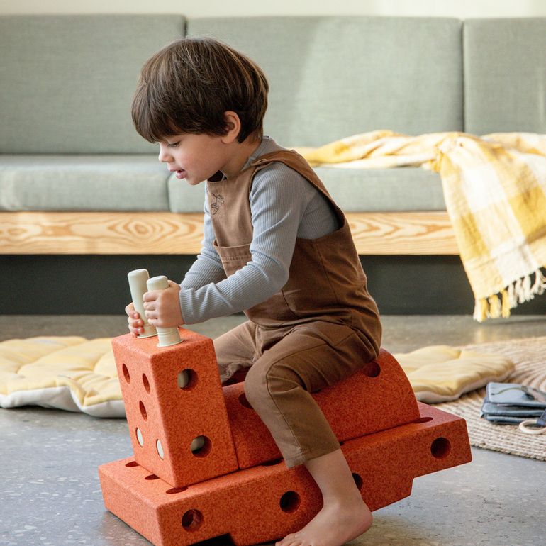 Kind zit op MODU Curiosity Set bouwblokken in burnt orange, balancerend op het speeltuig in woonkamer