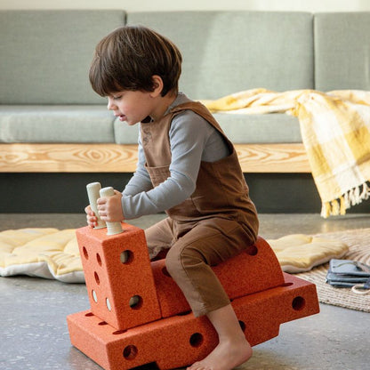 Kind zit op MODU Curiosity Set bouwblokken in burnt orange, balancerend op het speeltuig in woonkamer