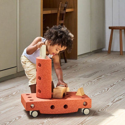 Kind speelt met MODU Curiosity Set bouwblokken in burnt orange, bouwt constructie met wielen op houten vloer