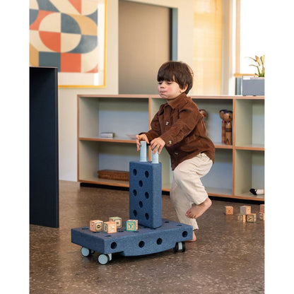 Peuter speelt met MODU Curiosity Set deep blue in speelkamer, balanceert op modulair bouwspeelgoed met blokken erboven