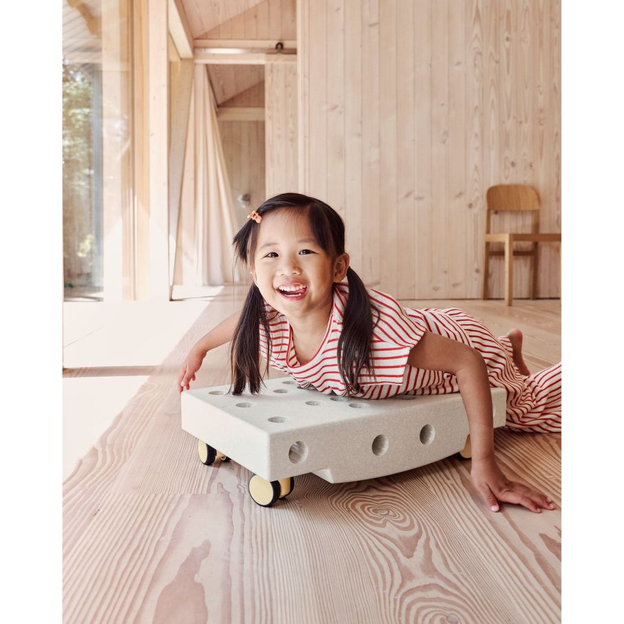 Meisje speelt met MODU Curiosity Set, liggend op houten vloer met het zandkleurige bouwspeelgoed met gele wieltjes
