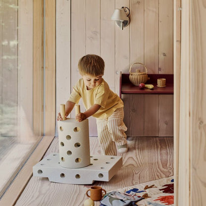 Peuter speelt met MODU Curiosity Set: wit holle cilinder met gaten op platform, vanaf bovenaanzicht in houten speelkamer.