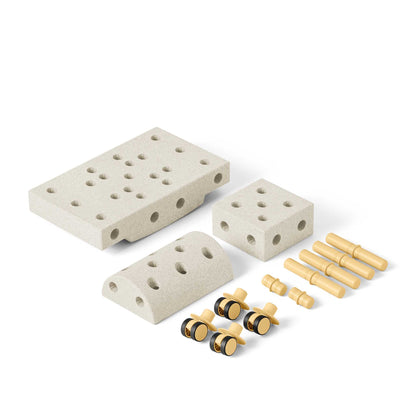 MODU Curiosity Set onderdelen uitgelegd: beige blokken met gaten, houten pennen en gele wielen met zwarte assen tegen witte achtergrond
