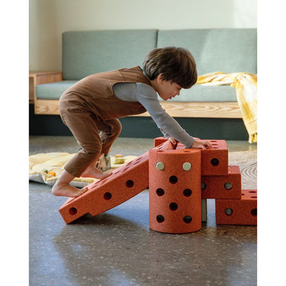 Kind bouwt met MODU Dreamer Set bouwblokken in burnt orange, glijbaan en kubussen met gaten, speelkamer achtergrond