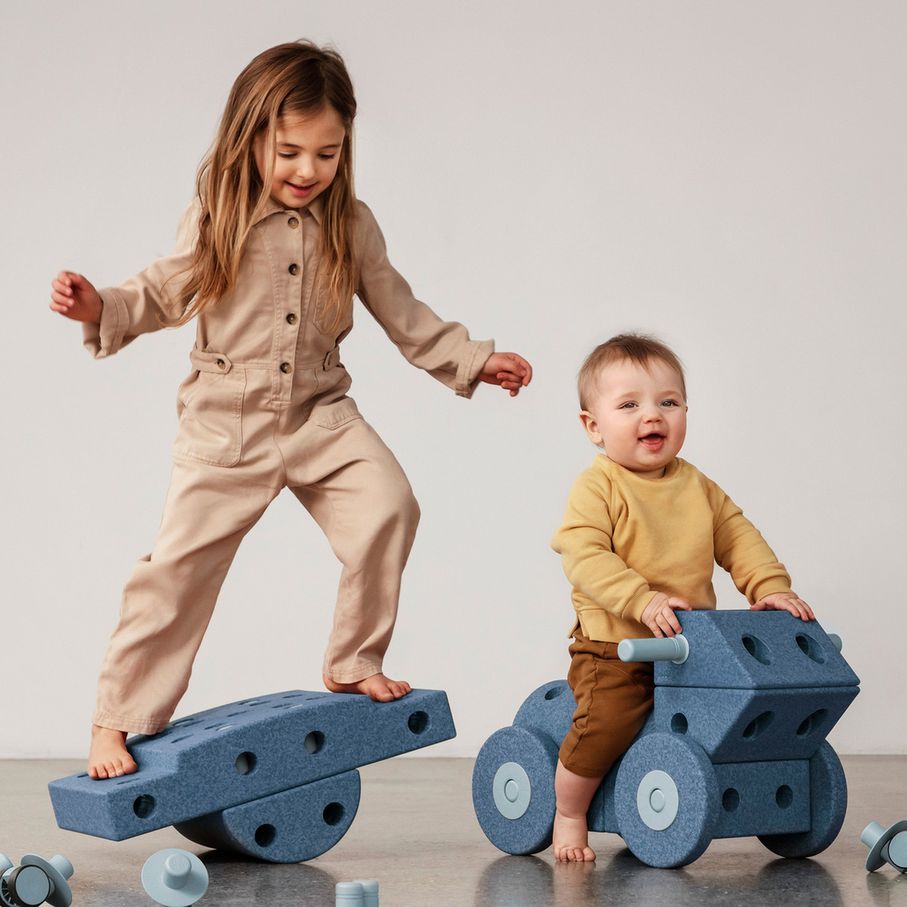 Twee kinderen spelen met MODU Dreamer Set bouwblokken in blauw; meisje balanceert op wip, kleuter zit op wieltjes-constructie.