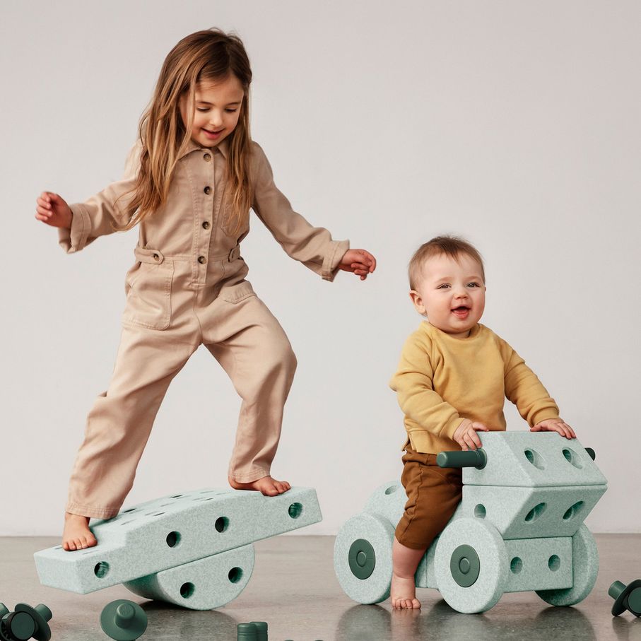 MODU Dreamer Set bouwblokken: twee kinderen spelen met modulaire schuimblokken en wielen, één kind balanceert op wipplank, ander kind zit op wieltjesv