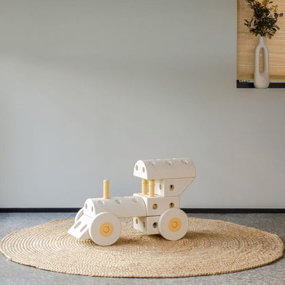 MODU Dreamer Set in wit en geel: bouwbare locomotief op rond juttapijt tegen minimalistisch interieur met plantendecoratie