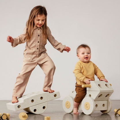 MODU Dreamer Set: twee kinderen spelen met zandgrijze schuimblokken en houtafwerking, één kind balanceert op een wiebelplank, ander kind zit op een wi