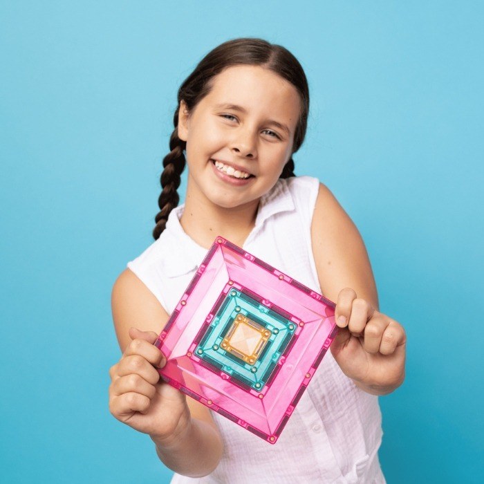 Meisje toont Connetix pastel portal pack magnetische tegels met nested vierkante frames in roze, turquoise en geel tegen blauwe achtergrond