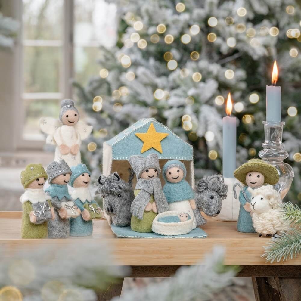 Sjaal met Verhaal kerststal wolvilt ijsblauw-wit met 11 figuren op houten tafel, vooraanzicht met brandende kaars en kerstboom op achtergrond