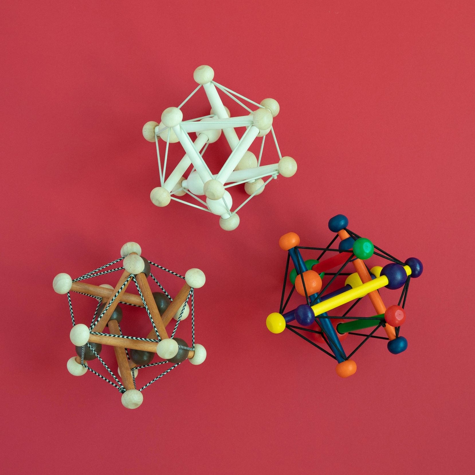 Manhattan Toy Skwish Classic rammelaar: drie verschillende modellen in crème, hout-touw en kleurrijke uitvoering op roze achtergrond