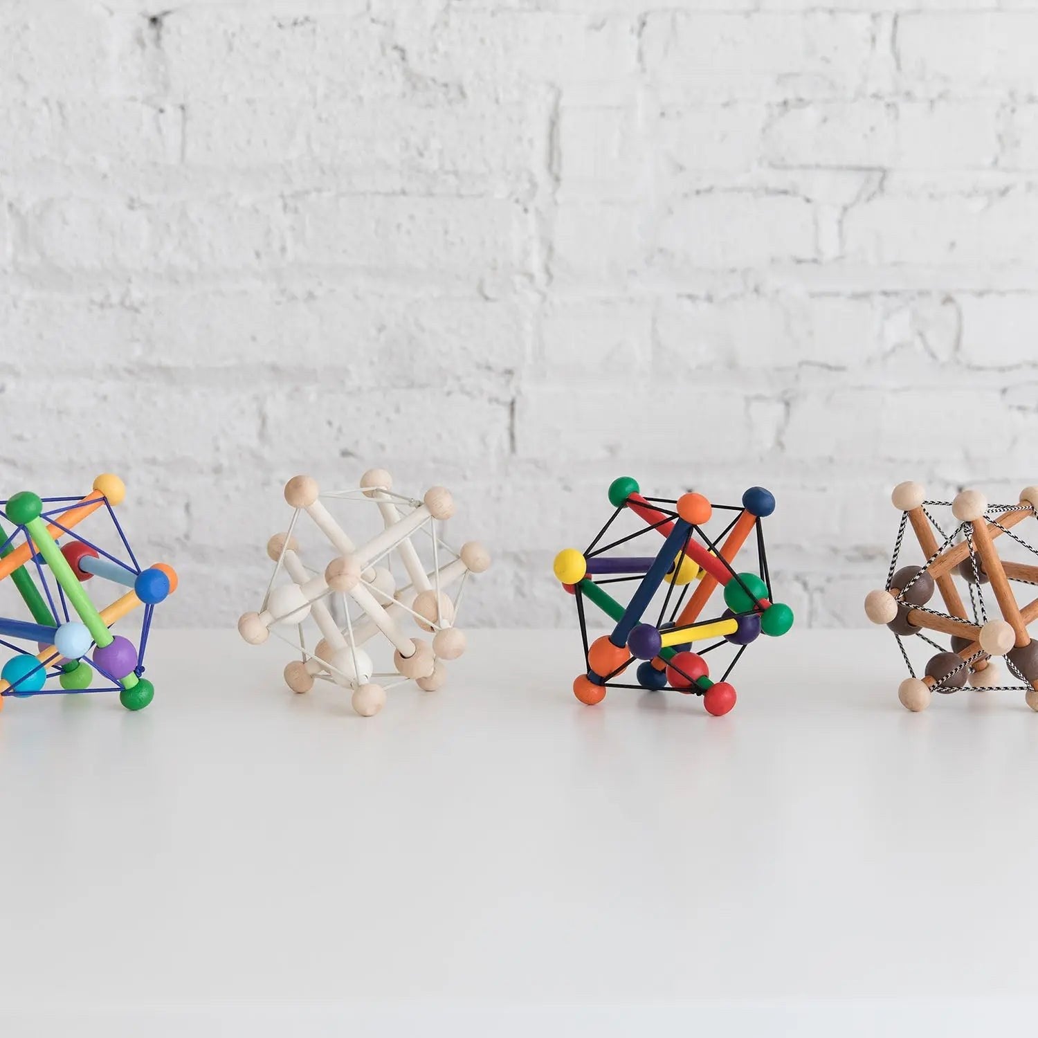 Manhattan Toy Skwish Color Burst rammelaar: vier varianten naast elkaar op wit oppervlak tegen bakstenen muur