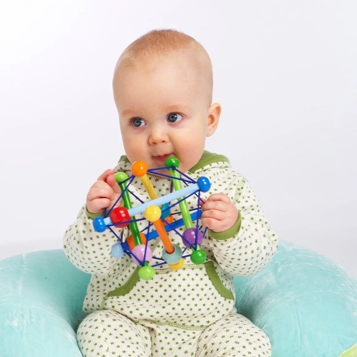 Manhattan Toy Skwish Color Burst rammelaar met gekleurde kralen in handen van zittend baby, frontaal zicht