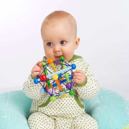 Manhattan Toy Skwish Color Burst rammelaar met gekleurde kralen in handen van zittend baby, frontaal zicht