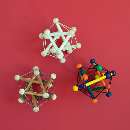 Manhattan Toy Skwish Natural rammelaar - drie modellen van houten grijpspeelgoed met elastische snaren in verschillende uitvoeringen op roze achtergro