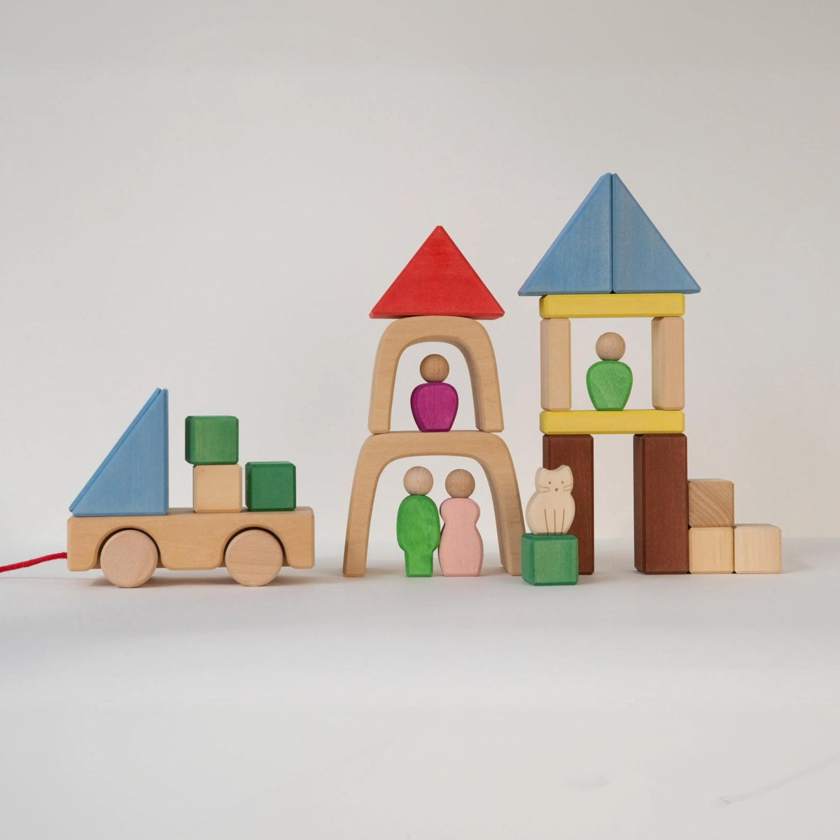 Avdar houten blokken speelset met drie architectuurcreaties naast elkaar: een wagentje, een toren met rode dak en twee figuren, en een blauwe torentje