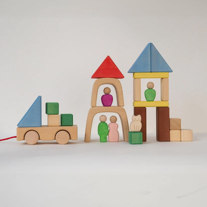 Avdar houten blokken speelset met drie architectuurcreaties naast elkaar: een wagentje, een toren met rode dak en twee figuren, en een blauwe torentje