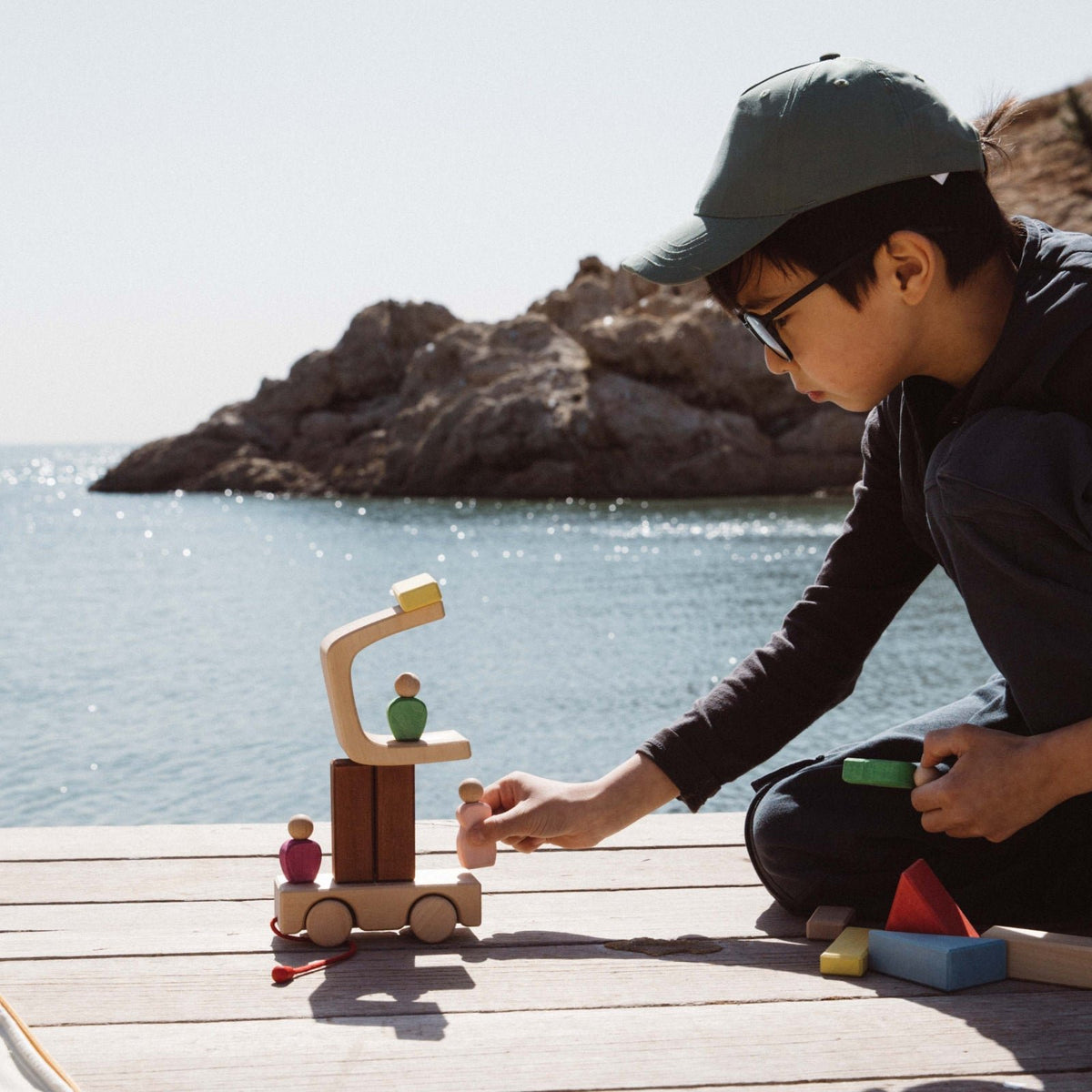 Avdar Trailer Travel Set: kind speelt met houten blokken en poppetjes aan zee met rotsformatie op achtergrond