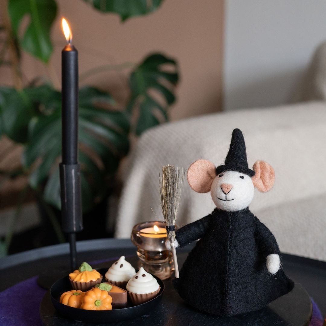 Sjaal met Verhaal vilten decoratie muis heks in zwart kostuum met bezem, omgeven door miniatuur halloween accessoires en brandende kaarsen.