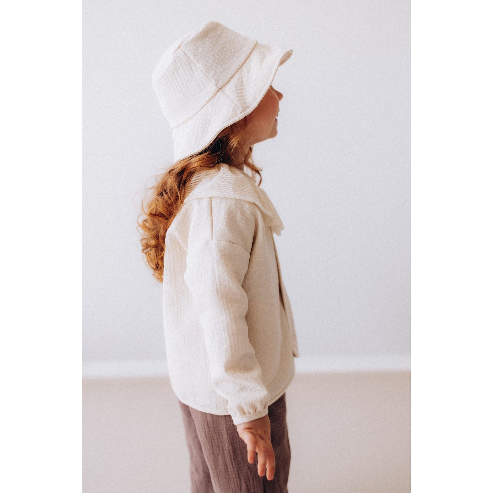 Wooly Organic vissershoedje in ecru, zijkant profiel met kind in wit linnen shirt