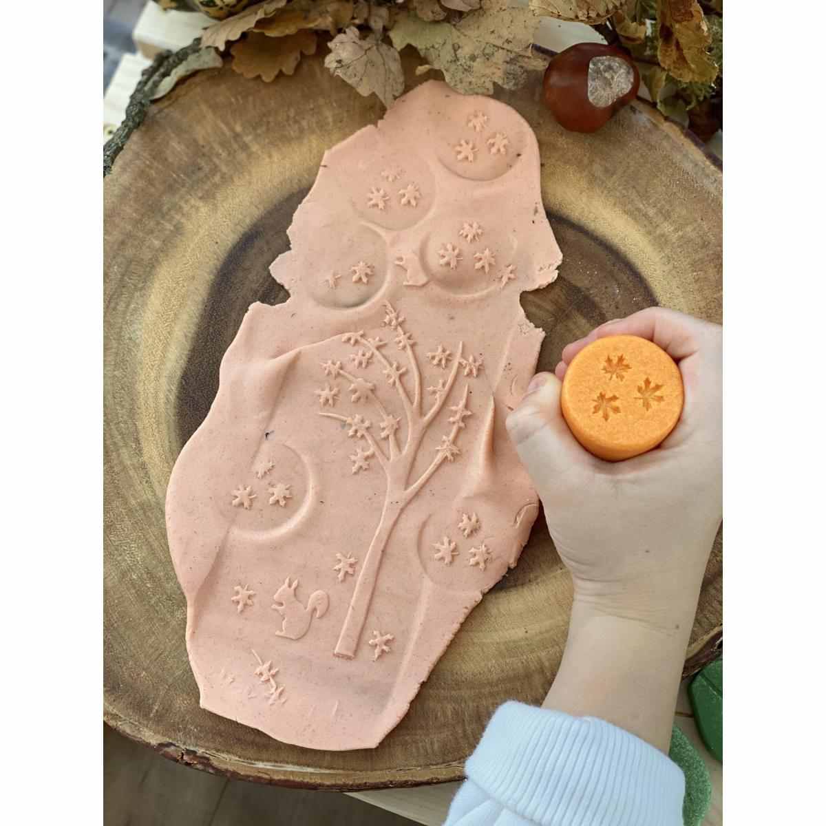 Yellow Door knetroller seizoenen set: hand houdt gele roller met sterpatronen boven roze kleiafdruk met bloemen- en maanmotieven op doek